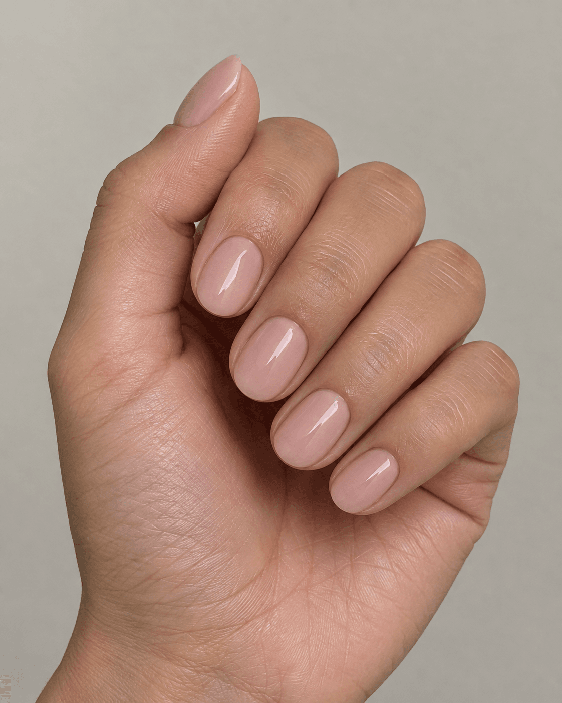 A photorealistic close-up beauty photograph of a hand with short, round-shaped acrylic nails painted in a soft blush-nude polish, neat and compact rounded tips.
