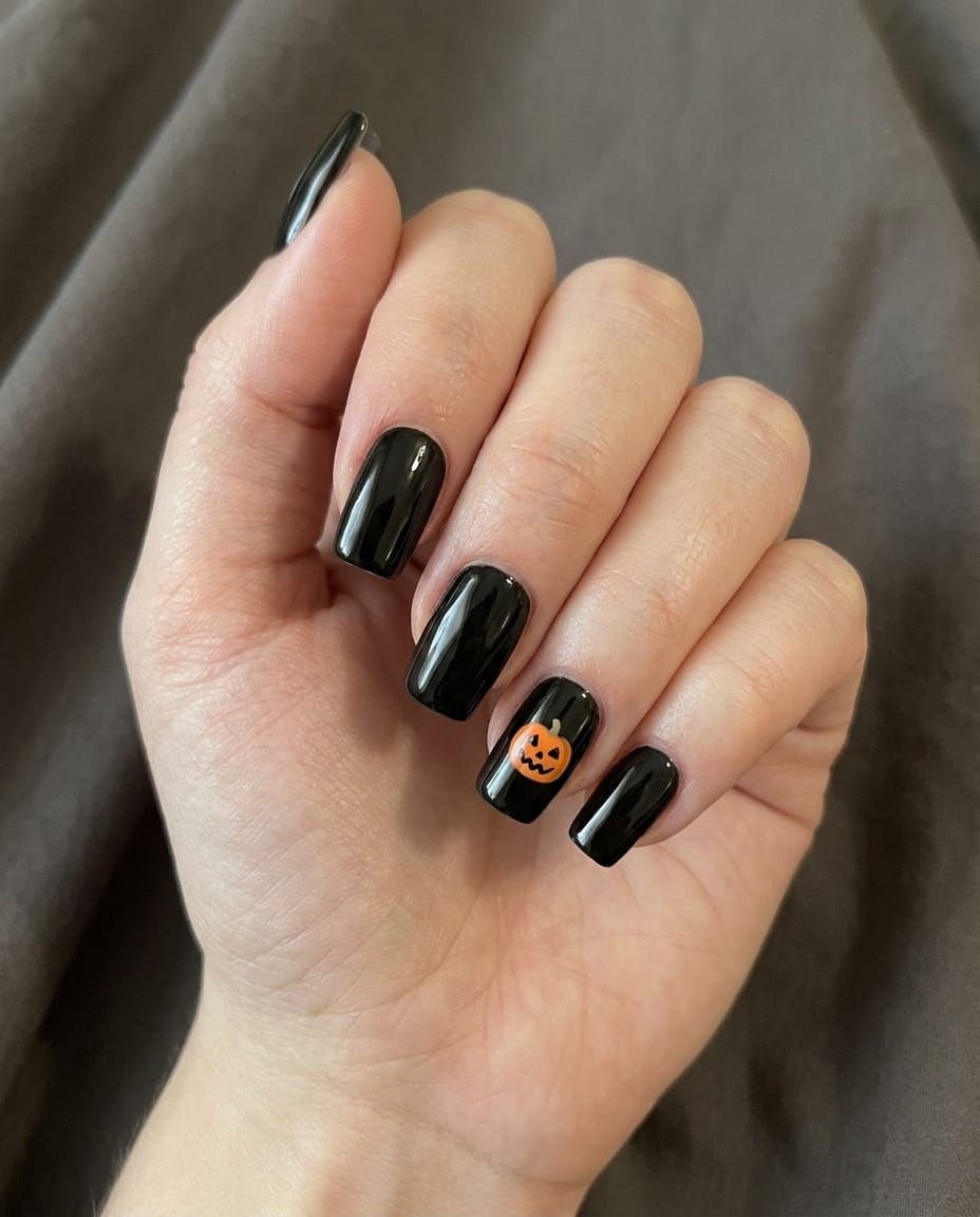 An elegant, photorealistic close-up beauty photograph of a slightly fuller, very pale hand with black square acrylic nails, featuring a tiny jack-o'-lantern accent on the ring finger: