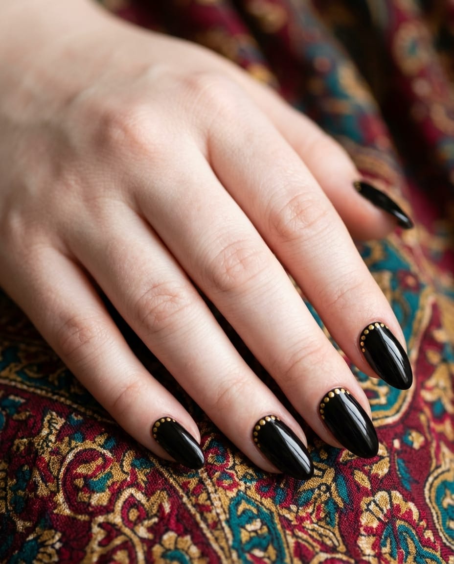 Hand with black acrylic nails featuring a gold dotted cuticle border