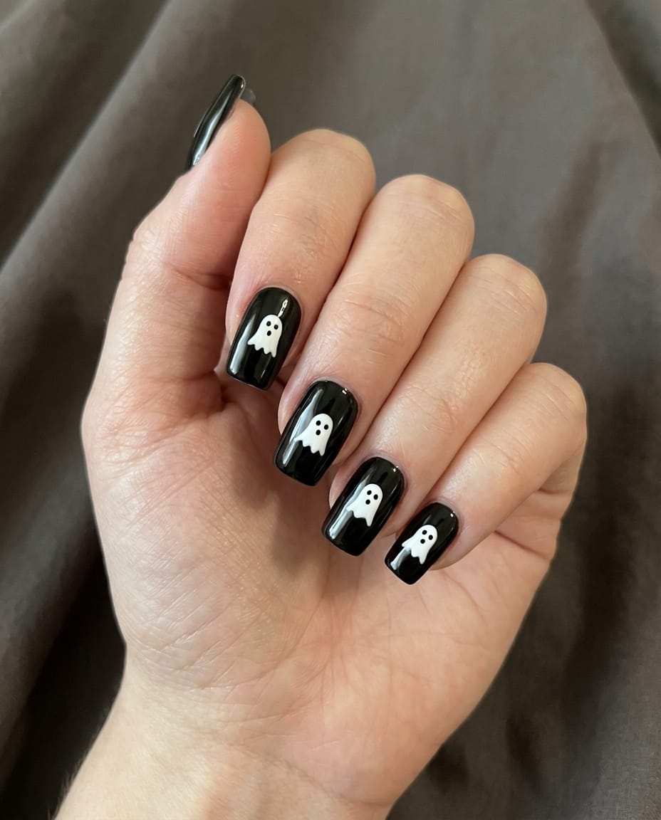 Hand with black acrylic nails featuring small white ghost silhouettes on every nail