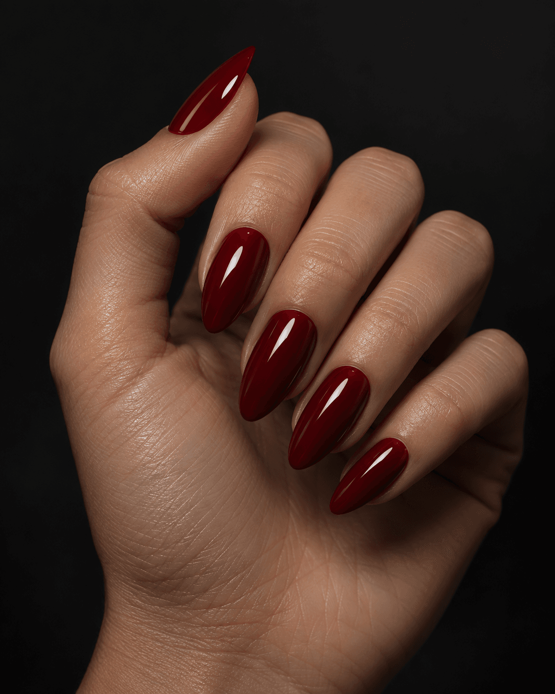 Hand with deep blood-red glossy almond acrylic nails.