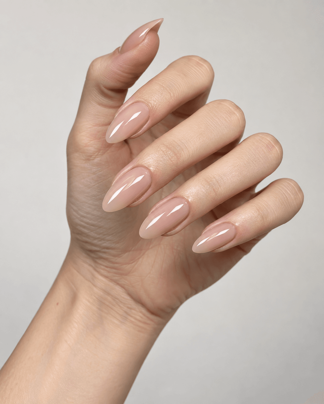 Hand with glossy, glass-like nude almond acrylic nails.