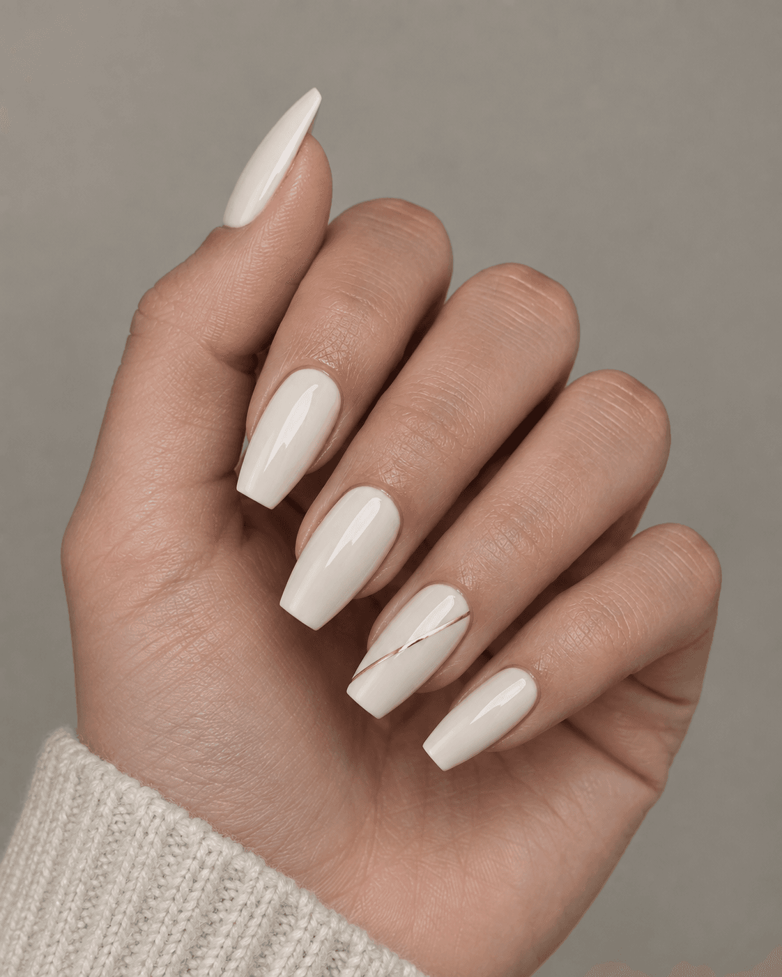 Hand with ivory acrylic nails and one diagonal gold line accent nail.