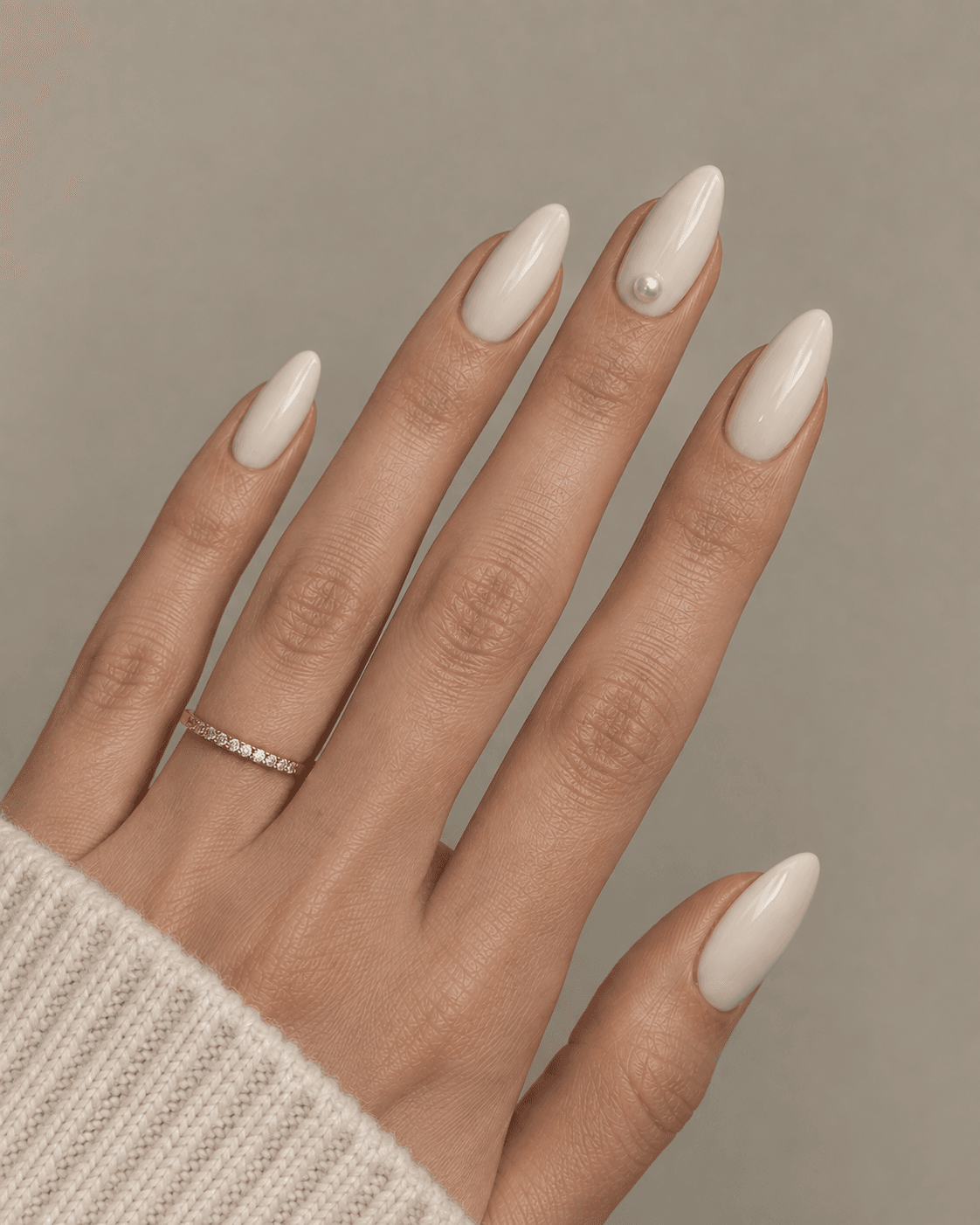 Hand with ivory acrylic nails featuring a single pearl embellishment on one nail.