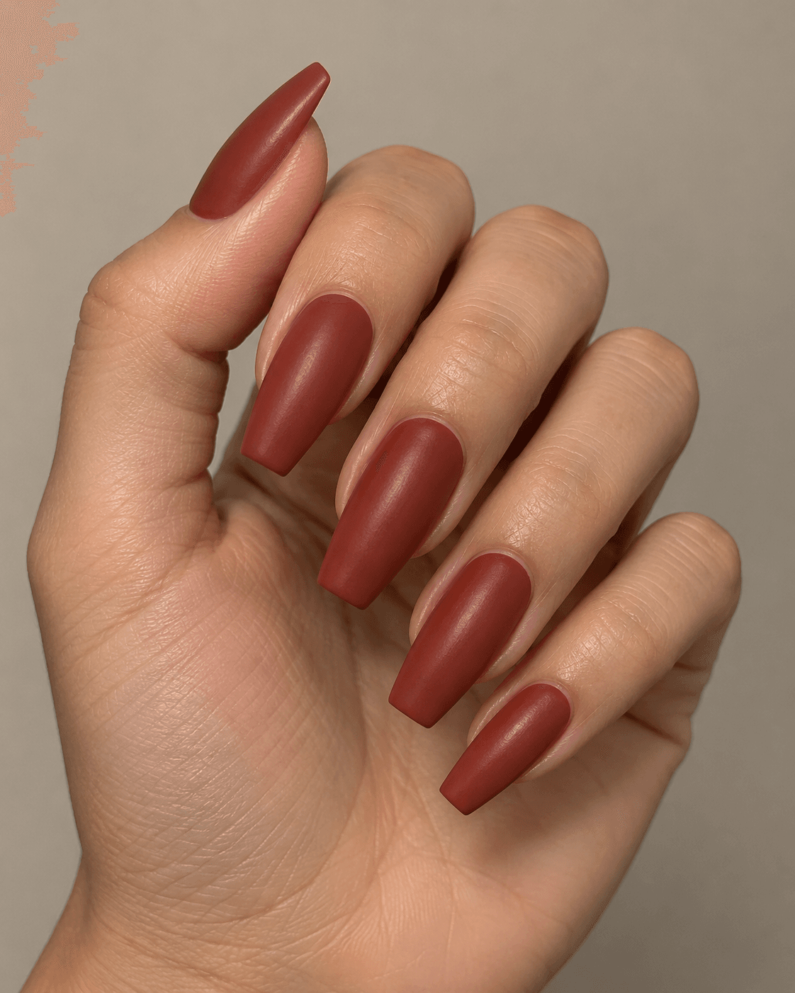 Hand with muted brick-red coffin-shaped acrylic nails.