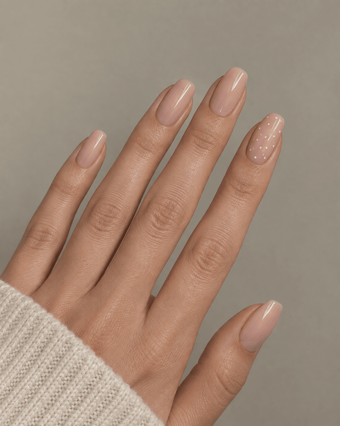 Hand with nude acrylic nails and one accent nail featuring scattered micro-dots.