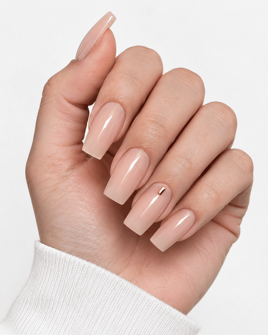 Hand with nude acrylic nails featuring a small gold rectangle accent.