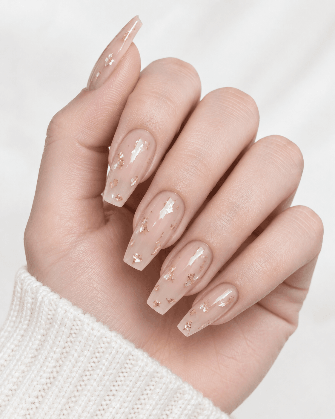 Hand with sheer nude acrylic nails featuring subtle gold foil flecks.