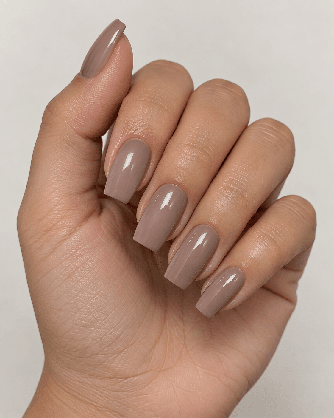 Hand with short-to-medium coffin-shaped nude acrylic nails.