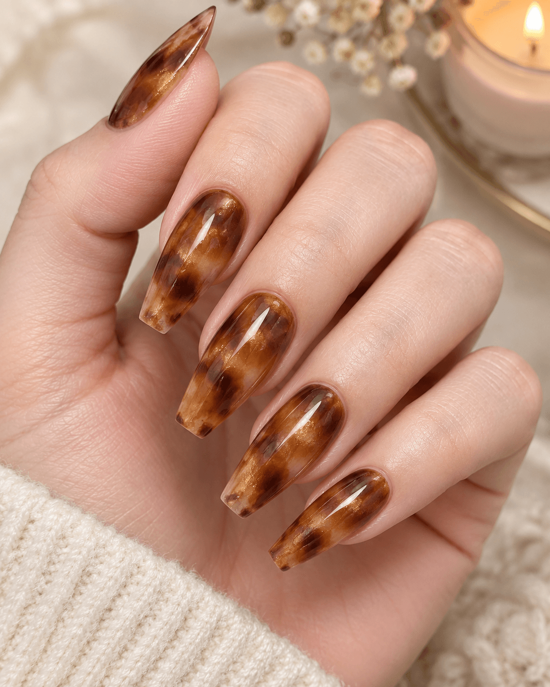 Hand with soft tortoiseshell-pattern acrylic nails in warm browns and golds.