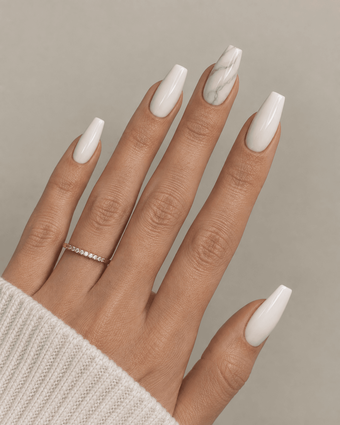 Hand with white acrylic nails and one marble-veined accent nail.